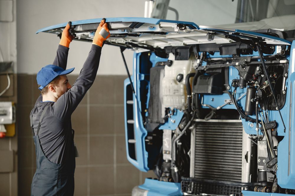 Technician lifting the front hood of a blue commercial truck to access the engine in a service shop